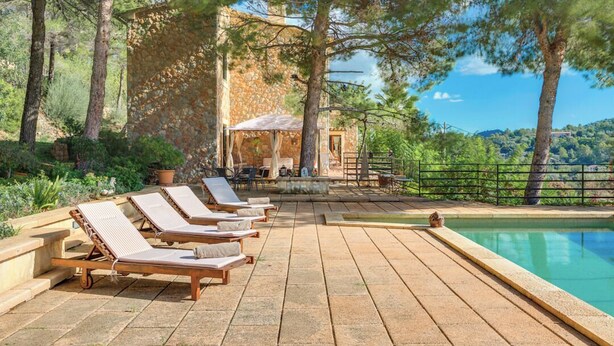 Zona junto a la piscina con sillas de descanso, un edificio de piedra y vistas del paisaje circundante.