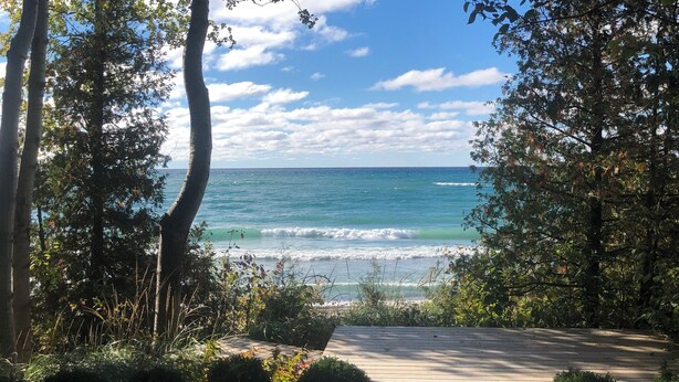 A wooden pathway leading to a beach with ocean views, surrounded by trees and greenery. - Lakefront Leisurely Hideaway - Private and Peaceful (Kincardine)