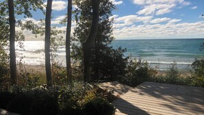 A wooden deck leading to a beach with ocean views, surrounded by trees and shrubs. - Lakefront Leisurely Hideaway - Private and Peaceful (Kincardine)
