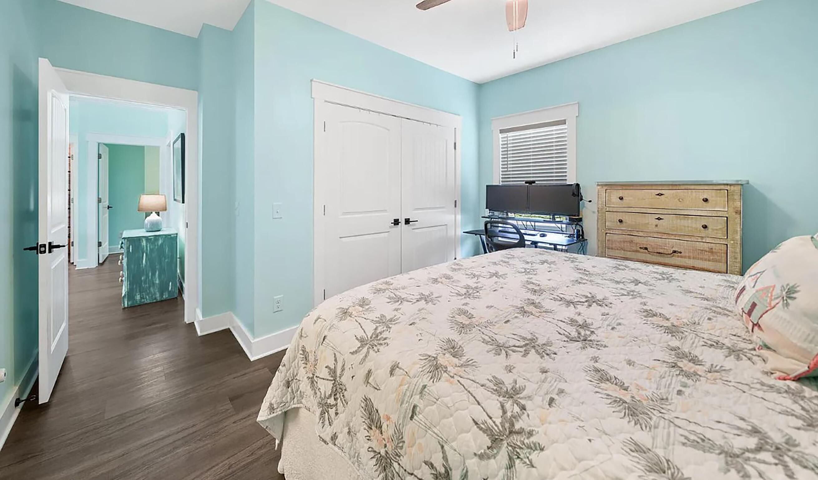 Une chambre à coucher comprenant un lit, une commode, un bureau et une porte donnant sur une autre pièce.