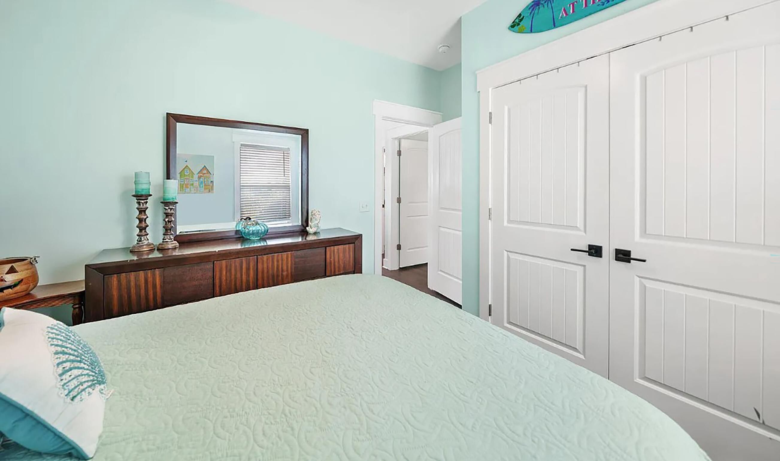 Un dormitorio con cama, cómoda, espejo y dos puertas.