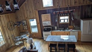 A rustic cabin interior with a wooden dining area, a kitchen with a central island, and a cozy living space with a leather couch. - Hidden Oaks Lavish Cabin #2 (Abbeville)