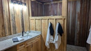 A rustic wooden bathroom with a sink, cabinets, and a shower area. - Hidden Oaks Lavish Cabin #2 (Abbeville)
