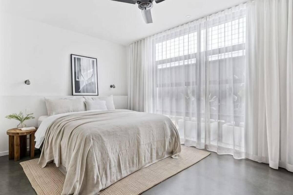 Un dormitorio moderno con una cama grande, cortinas traslúcidas y un ventilador de techo.
