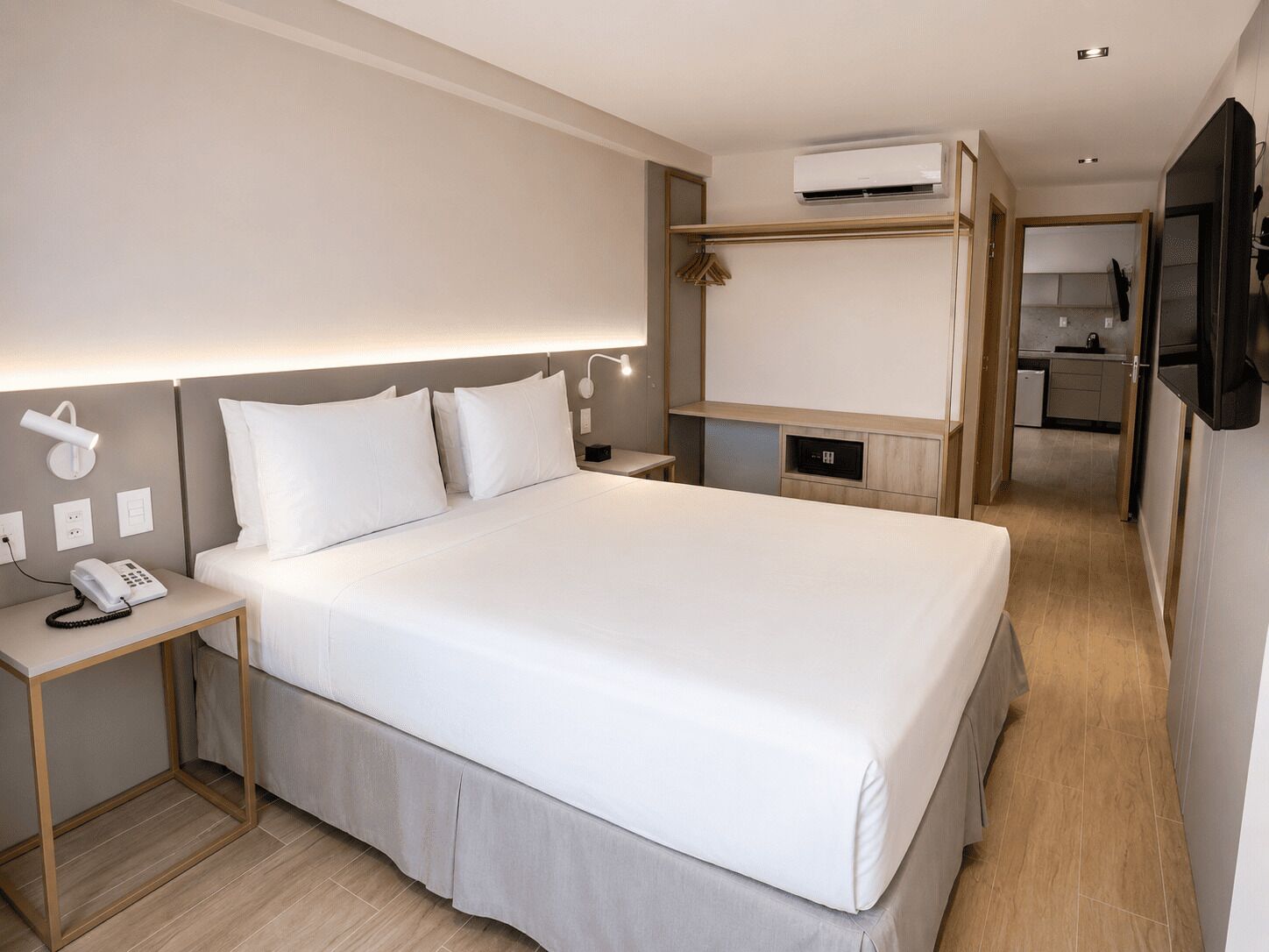 Habitación de hotel con una cama grande, mesita de noche con teléfono, lámpara de escritorio, unidad de aire acondicionado y vista al área de la cocina.