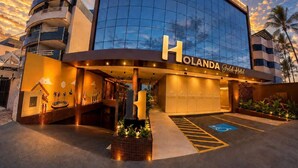 A modern hotel with a curved facade, a prominent 'HOLANDA Gold Hotel' sign, and a disabled parking space. - Holanda Gold Hotel Praia de Tambaú (João Pessoa)
