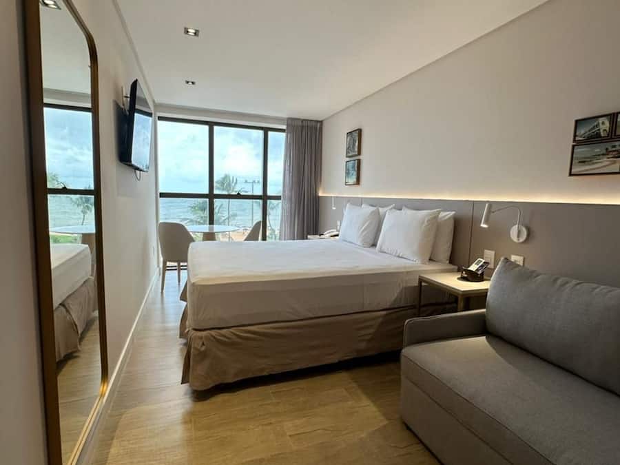 A hotel room with a bed, a sofa, a desk, a chair, and a view of the ocean.