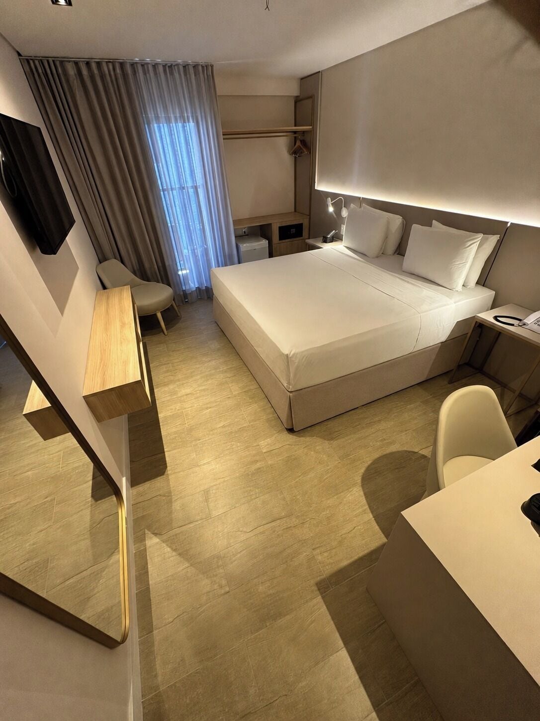 A modern hotel room with a bed, desk, chair, and a small table.