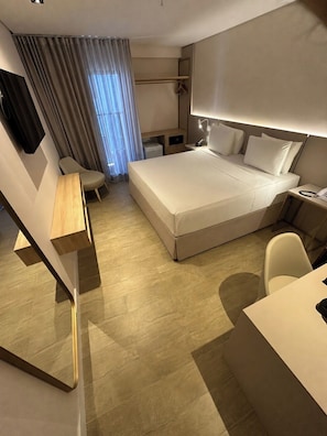 Quarto de hotel moderno com cama, escrivaninha, cadeira e uma pequena mesa.