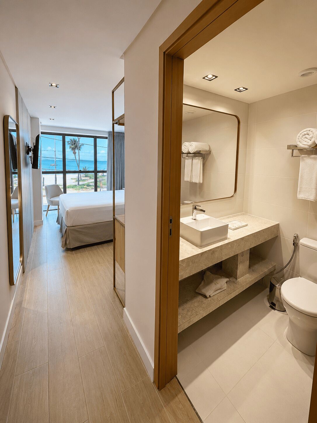 A modern hotel room with a large bed, a bathroom with a mirror, and a view of the sea.