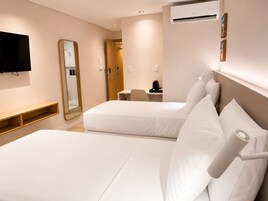 Habitación de hotel con dos camas, televisión, espejo, escritorio y aire acondicionado.