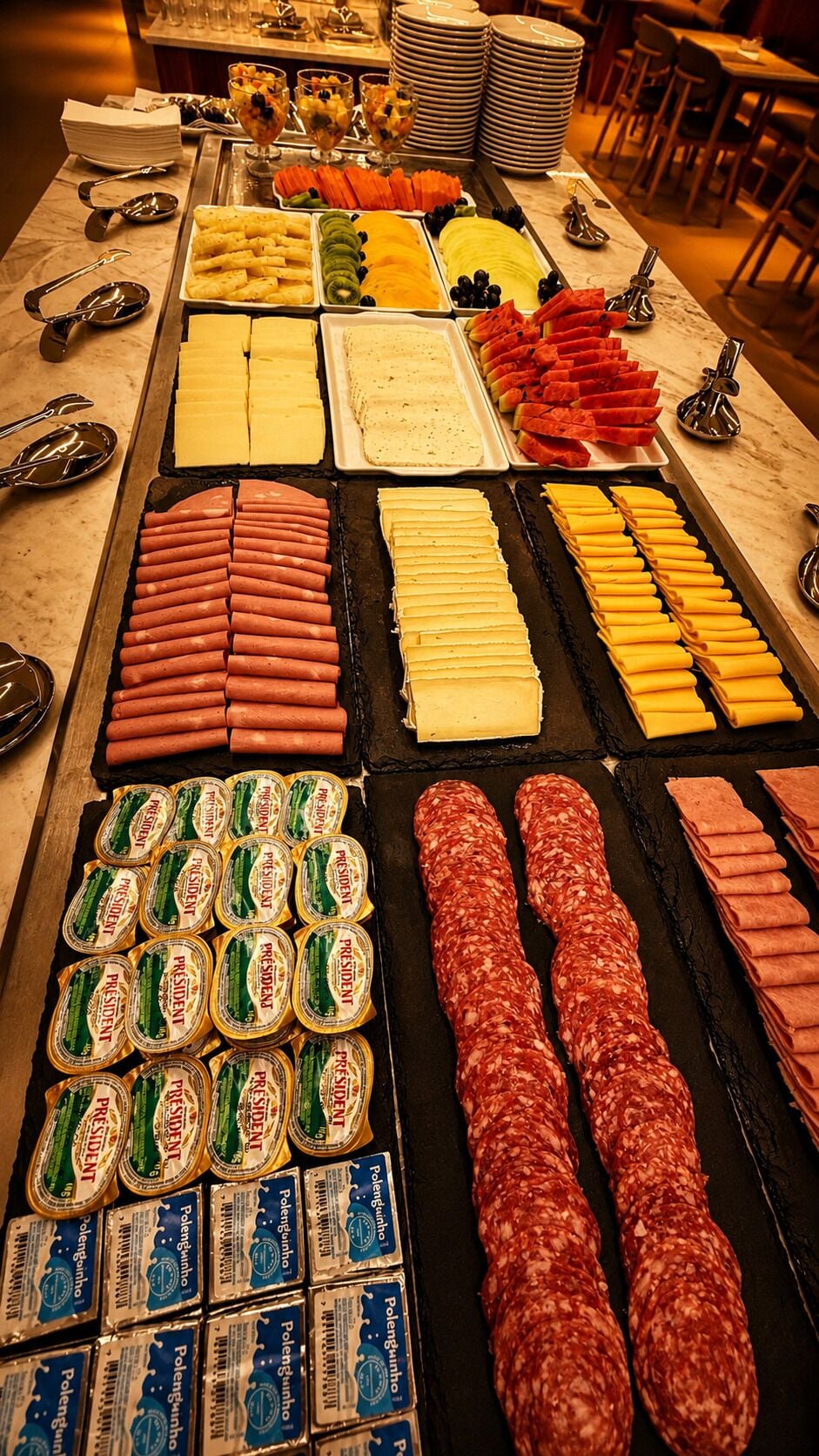 Noutopöydässä on tarjolla monenlaista ruokaa, kuten hot dog -leipiä, juustoa ja viipaloituja lihaleikkeleitä.
