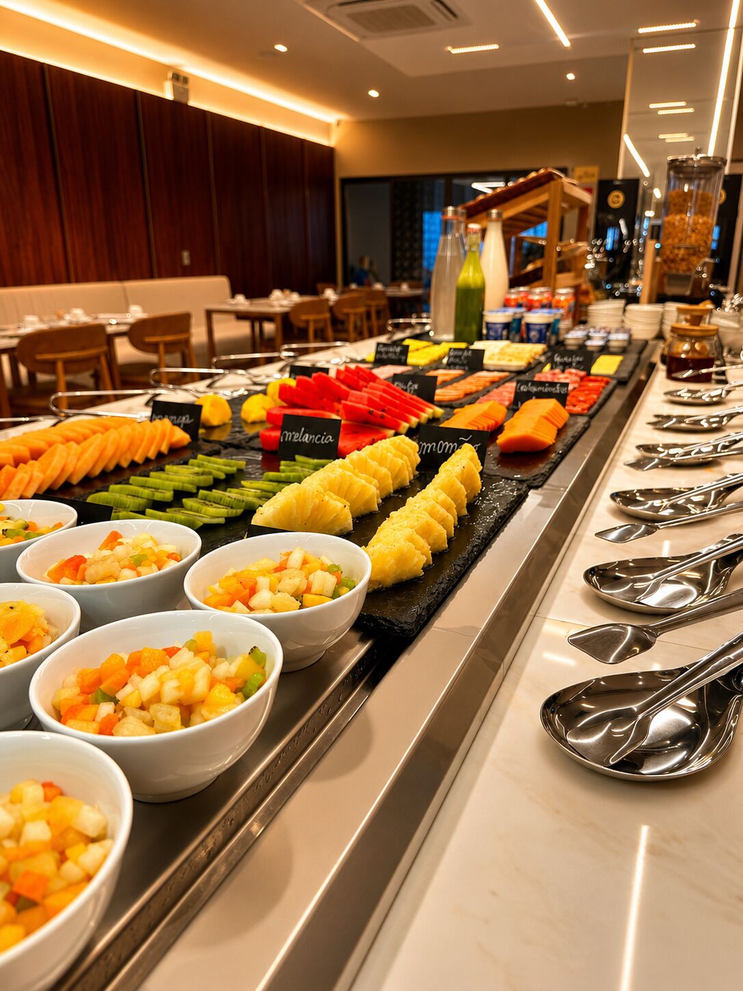 A buffet with various fruits and vegetables, including melon, pineapple, and carrots, arranged on a counter with serving utensils.