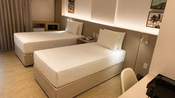A hotel room with two beds, a desk, a chair, a phone, and a small table with a lamp.
