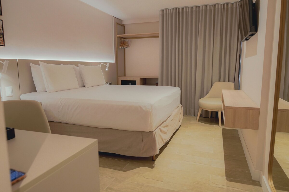Ein Hotelzimmer mit einem großen Bett, einem Schreibtisch, einem Stuhl, einem Fernseher und einem Kleiderschrank.