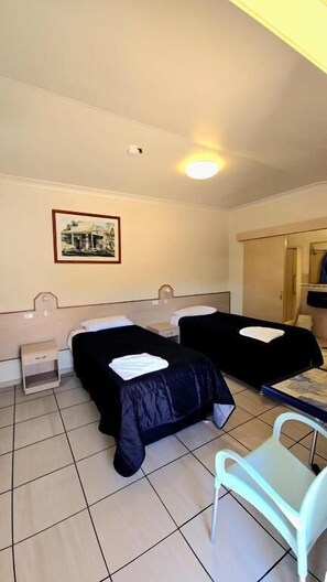 A room with two beds, a desk, a chair, a framed picture on the wall, and a ceiling light. - Royal Motel Rockhampton (Allenstown)