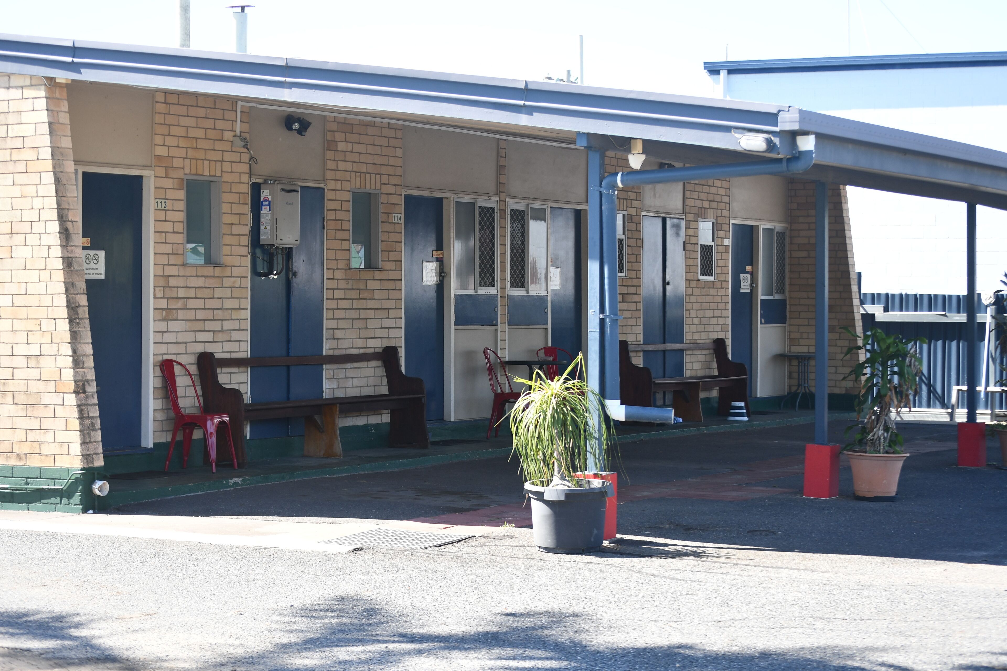 A motel with a covered outdoor seating area, a brick facade, and a few potted plants.