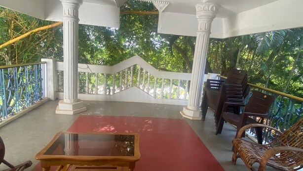 A covered balcony with a red carpet, white columns, wicker chairs, and a glass table. - Charming 4-bedroom villa with AC and WiFi in enchanting Bommayapalayam Peaceful, (Bommayapalayam)