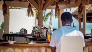 Zona de bar con mostrador de piedra, diversas botellas y vista a la playa.