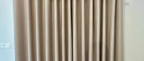 A beige curtain with a rod, a light switch, and a marble floor.