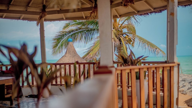 Un pabellón frente a la playa con techo de paja, barandilla de madera y plantas en macetas.