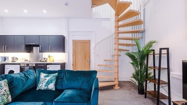 Uma sala de estar moderna com um sofá verde-água, uma mesa de centro de madeira e uma escada em espiral que dá para um andar superior.