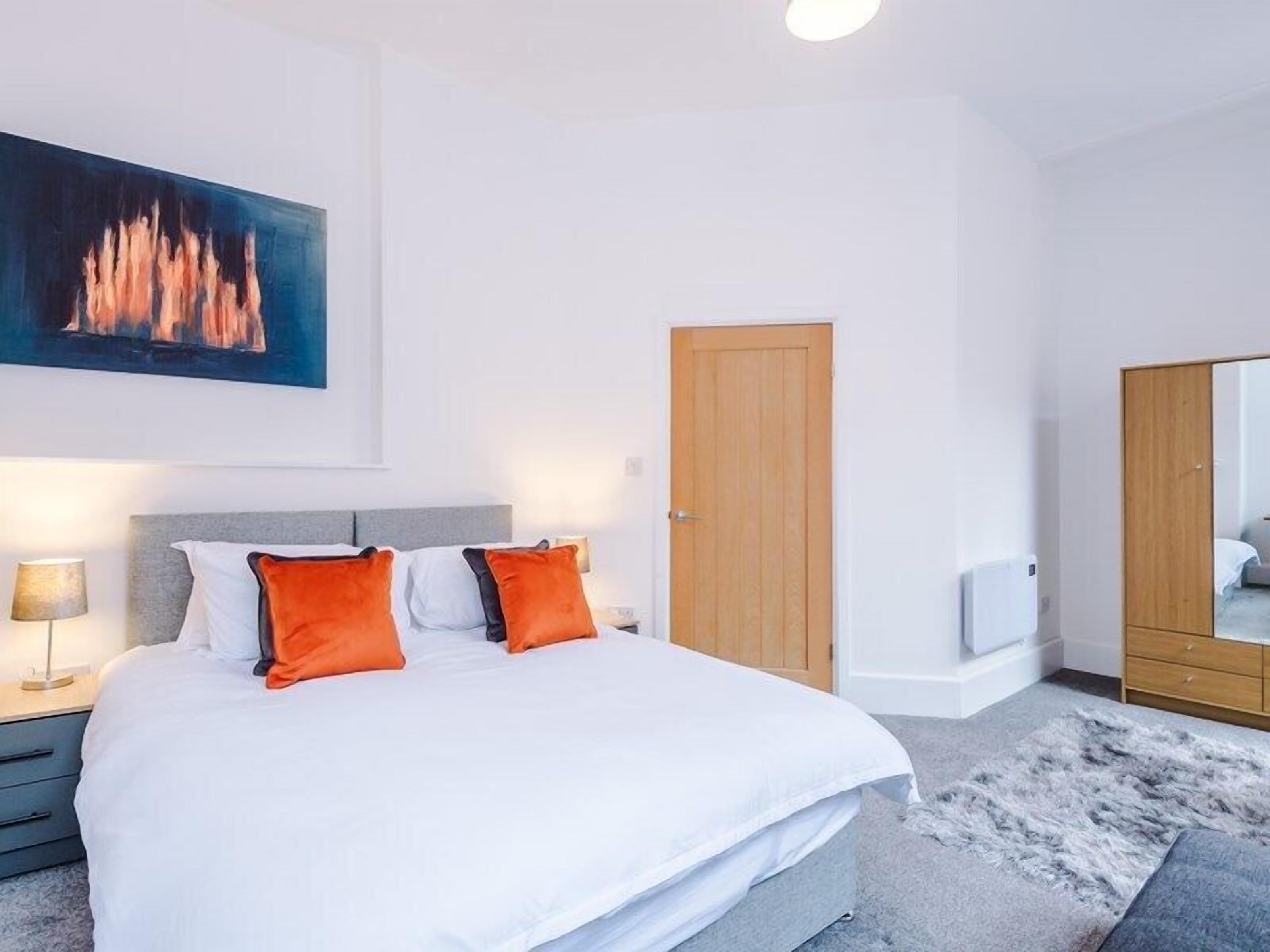 Een slaapkamer met een bed, een houten deur, een spiegel en een schilderij aan de muur.