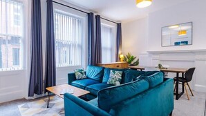 Uma sala de estar moderna com um sofá verde-água, uma mesa de centro de madeira e uma área de refeições com uma mesa pequena e cadeiras.