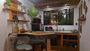 Une cuisine compacte avec des étagères en bois, un coin bar et une fenêtre donnant sur les arbres.