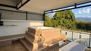 Un área de estar moderna al aire libre con un banco de madera y una mesa, con vistas a un paisaje verde y exuberante.