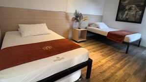 Habitación de hotel con dos camas, cabecera de madera, mesita de noche con un florero y un cuadro en la pared.
