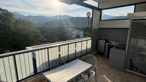 Un balcón con mesa y sillas, una pequeña cocina y vistas a montañas.