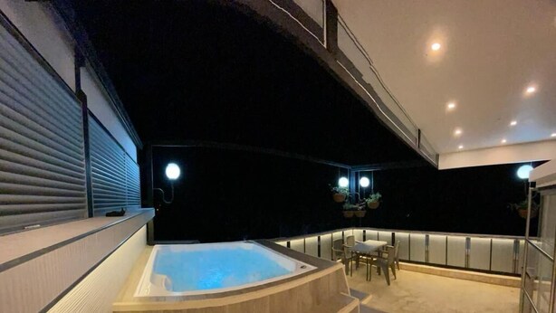 Un área moderna de piscina interior con un jacuzzi, asientos y una escalera que lleva a un nivel superior.