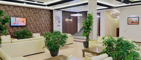 A modern lobby with sofas, a TV, and potted plants.