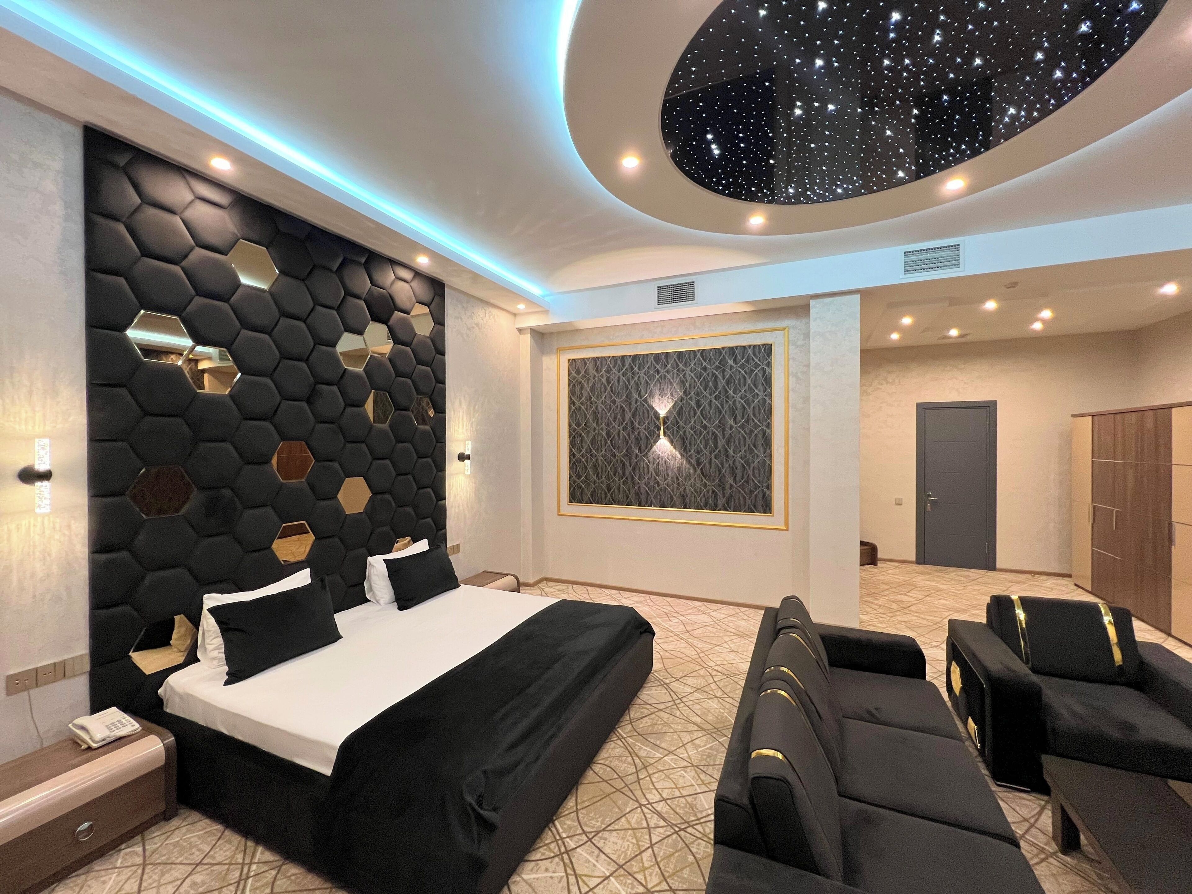A modern hotel room with a large bed, a seating area, and a unique ceiling design.