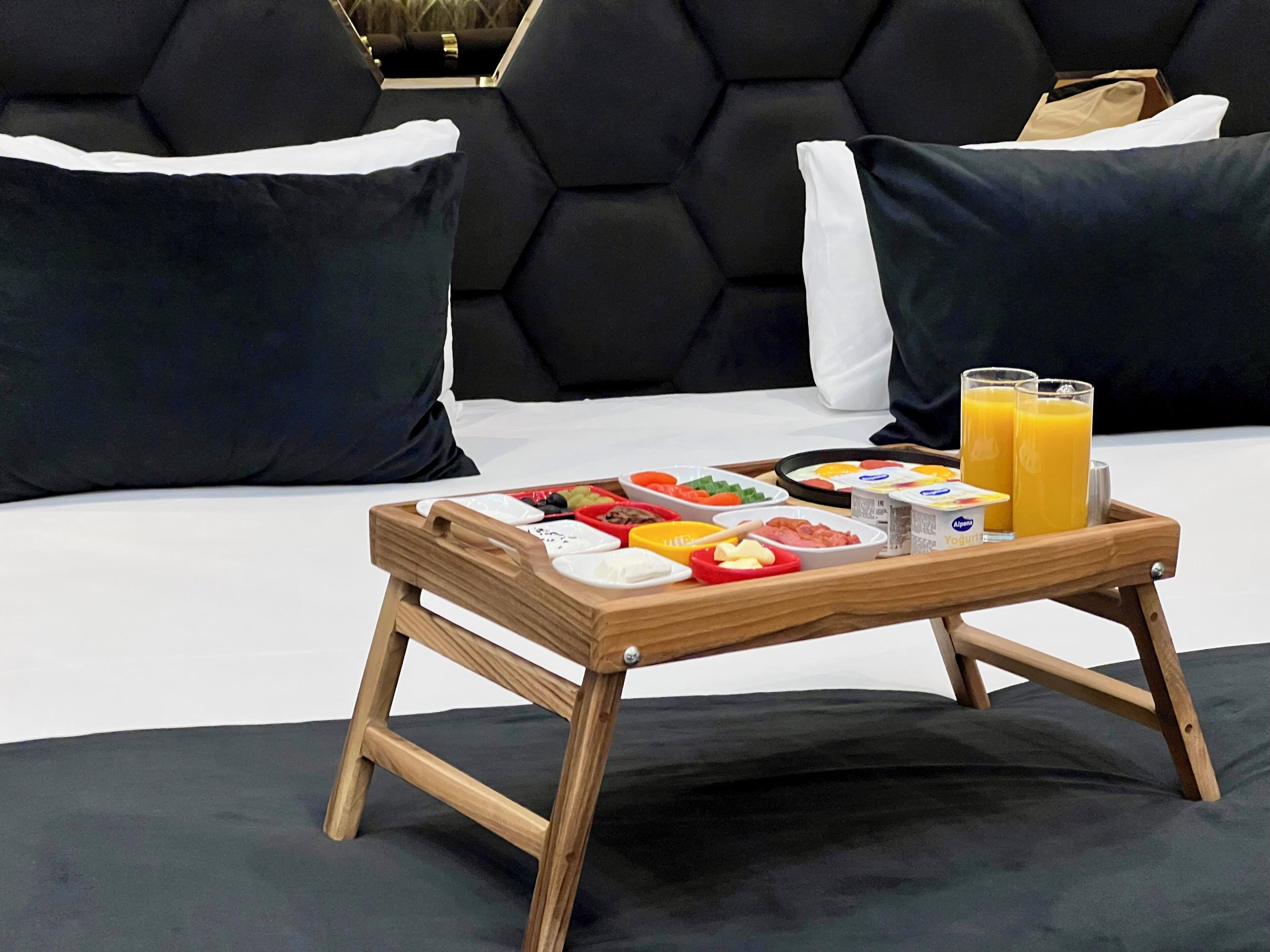 Ein Frühstücksbrett mit verschiedenen Speisen und zwei Gläsern Orangensaft auf einem Bett mit schwarz-weißer Bettwäsche.