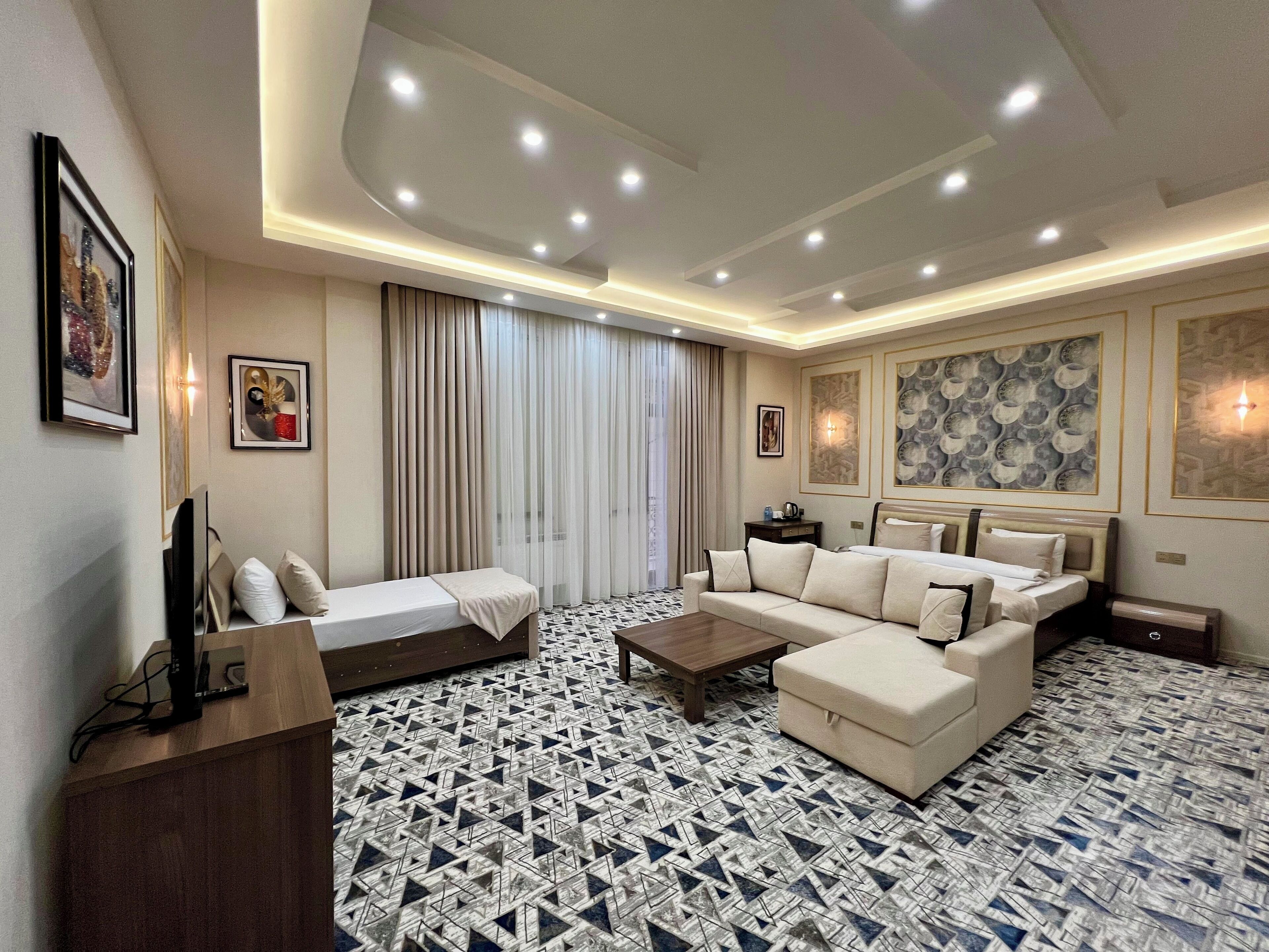 A modern hotel room with a sofa set, a bed, a coffee table, and patterned flooring.