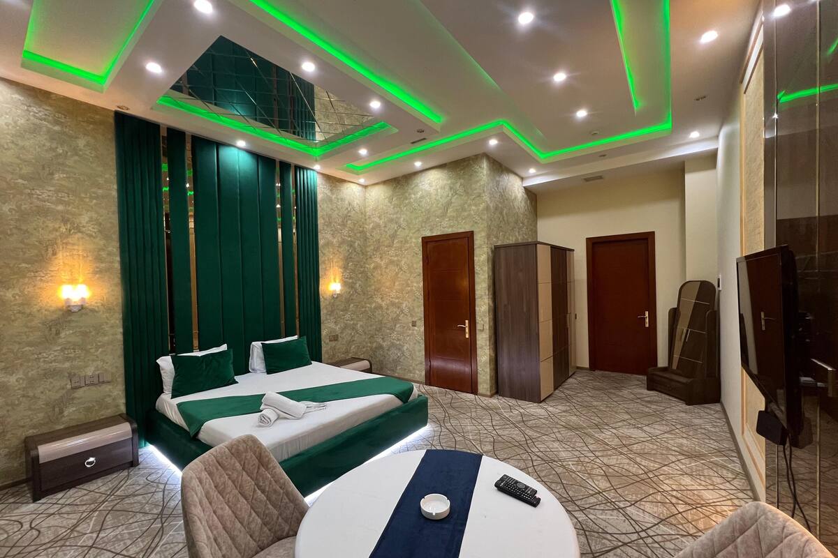 A hotel room with a bed, two bedside tables, a chair, a small table, and a television.