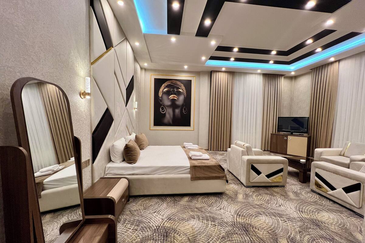 A modern bedroom with a large bed, a sitting area, a TV, and a mirror.