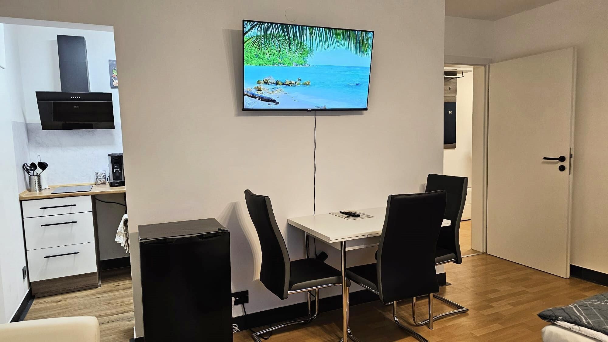 Moderni keittiö, jossa on sisäänrakennettu liesi, kahvinkeitin ja seinälle asennettu televisio, josta näkyy kuva rannasta.