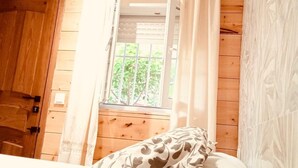Ein Schlafzimmer mit Holzwänden, einem Fenster mit Vorhängen und einem Bett mit gemusterten Betttextilien.