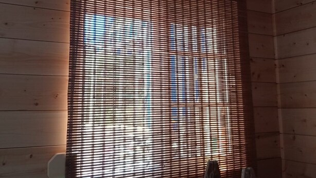 Ein Zimmer mit Holzwandverkleidung, einem Fenster mit Lamellenjalousien und einer an der Wand angelehnten Leiter.