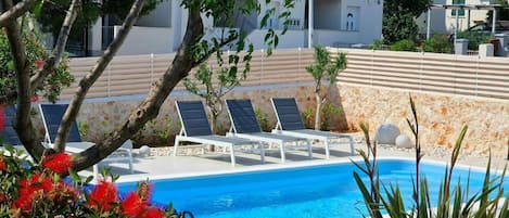 Zona de piscina amb gandules i una paret de pedra.