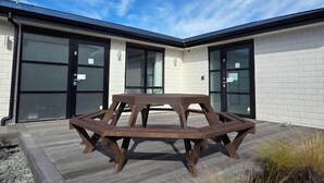 A wooden picnic table in front of a building with large windows and a satellite dish. - Snowy Peak Apartment (Lake Tekapo)