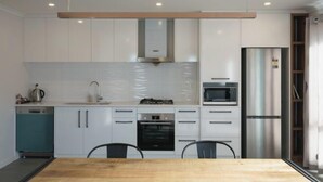 A modern kitchen with white cabinets, a stainless steel refrigerator, a microwave, and a dishwasher. - Snowy Peak Apartment (Lake Tekapo)