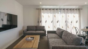 A living room with two sofas, a coffee table, a flat-screen TV, and a dining area with chairs. - Snowy Peak Apartment (Lake Tekapo)