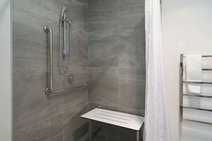 Ducha con cabezal de ducha de mano, grifo empotrado en la pared y asiento de ducha con mampara de vidrio.
