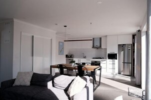 Uma sala de estar moderna com um sofá, uma mesa de jantar e uma cozinha ao fundo.