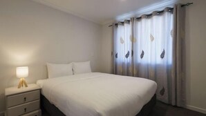 A bedroom with a bed, a nightstand with a lamp, and curtains. - Snowy Peak Apartment (Lake Tekapo)