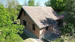 A small, single-story brick house with a sloped roof, surrounded by lush greenery.